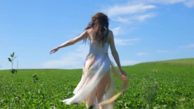 Beyaz elbiseli bir kadın yeşil bir arazide geziniyor. Beyaz elbiseli bir kadın huzurlu bir çayırda zarifçe yürüyor. Huzurlu sahne: Beyaz elbiseli kadın, mavi gökyüzüne karşı tarlada gülümsüyor ve geziniyor. Sakin bir an: zarif giyinmiş kadın 