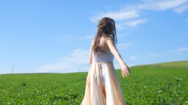 Beyaz elbiseli bir kadın yeşil bir arazide geziniyor. Beyaz elbiseli bir kadın huzurlu bir çayırda zarifçe yürüyor. Huzurlu sahne: Beyaz elbiseli kadın, mavi gökyüzüne karşı tarlada gülümsüyor ve geziniyor. Sakin bir an: zarif giyinmiş kadın 