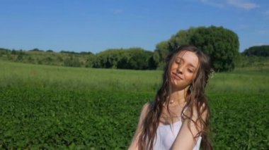 Beyaz elbiseli bir kadın yeşil bir arazide geziniyor. Beyaz elbiseli bir kadın huzurlu bir çayırda zarifçe yürüyor. Huzurlu sahne: Beyaz elbiseli kadın, mavi gökyüzüne karşı tarlada gülümsüyor ve geziniyor. Sakin bir an: zarif giyinmiş kadın 