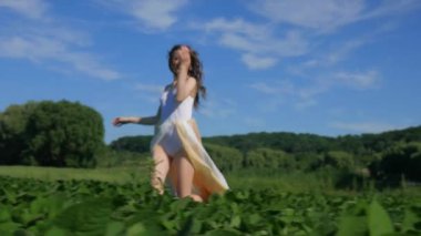 Beyaz elbiseli bir kadın yeşil bir arazide geziniyor. Beyaz elbiseli bir kadın huzurlu bir çayırda zarifçe yürüyor. Huzurlu sahne: Beyaz elbiseli kadın, mavi gökyüzüne karşı tarlada gülümsüyor ve geziniyor. Sakin bir an: zarif giyinmiş kadın 