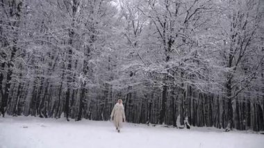 Beyaz atkı ve paltolu kadın karlı ormanda duruyor. Karla kaplı ormanda duran bir kadın. Kış sahnesinde beyaz önlüklü bir kadın kış ormanında yürüyor. Karlı orman manzarasında bir kadın. Beyaz önlüklü bir kadınla karlı orman arkaplanı. 