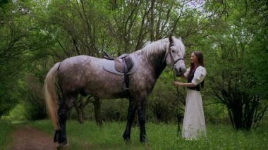 Huzurlu orman ortamında at besleyen bir kadın. Kadının yürüdüğü ve atla ağaçlar arasında bağ kurduğu huzurlu bir an. Sakin orman sahnesinde at ve kadın arasındaki bağ. Tarlada atlara sevgi gösteren bir kadın. At okşayan kadın. 