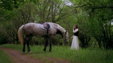 Huzurlu orman ortamında at besleyen bir kadın. Kadının yürüdüğü ve atla ağaçlar arasında bağ kurduğu huzurlu bir an. Sakin orman sahnesinde at ve kadın arasındaki bağ. Tarlada atlara sevgi gösteren bir kadın. At okşayan kadın. 