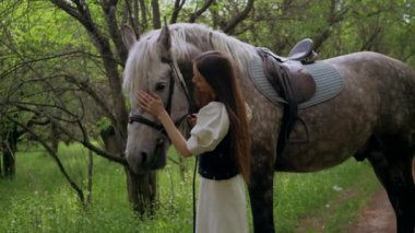 Huzurlu orman ortamında at besleyen bir kadın. Kadının yürüdüğü ve atla ağaçlar arasında bağ kurduğu huzurlu bir an. Sakin orman sahnesinde at ve kadın arasındaki bağ. Tarlada atlara sevgi gösteren bir kadın. At okşayan kadın. 
