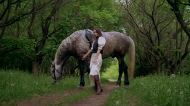 Huzurlu orman ortamında at besleyen bir kadın. Kadının yürüdüğü ve atla ağaçlar arasında bağ kurduğu huzurlu bir an. Sakin orman sahnesinde at ve kadın arasındaki bağ. Tarlada atlara sevgi gösteren bir kadın. At okşayan kadın. 
