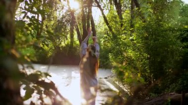 Nehirdeki bir teknede çiçek açan bir kadının sakin bir görüntüsü. Ulusal kıyafetli bir kadın ormanın ortasında canlı çiçeklerle dolu bir teknede kürek çekiyor. Rengarenk çiçeklerin arasında sakin bir tekne gezintisi yapan bir bayan.