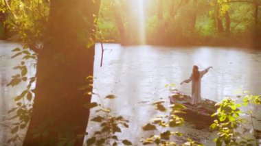 Nehirdeki bir teknede çiçek açan bir kadının sakin bir görüntüsü. Ulusal kıyafetli bir kadın ormanın ortasında canlı çiçeklerle dolu bir teknede kürek çekiyor. Rengarenk çiçeklerin arasında sakin bir tekne gezintisi yapan bir bayan.