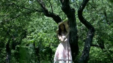 Bahçedeki ağaçların arasında duran pembe elbiseli ve hasır şapkalı kız. Park ortamında gülümseyen pembe elbiseli genç bir kız. Ormanda ağaçlarla çevrili pembe elbiseli bir kız. Pembe elbiseli kız yemyeşil ormanda dikiliyor.. 