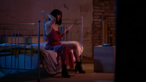 穿着红色长袍的女士躺在床上休息 穿着衣服的性感女人躺在一间黑暗的房间里的旧床上 穿着红色衣服的孤寂优雅的女士躺在床上 在浪漫而亲密的气氛中 穿着深红色衣服的女人躺在床上 迷人的女士 — 图库视频影像