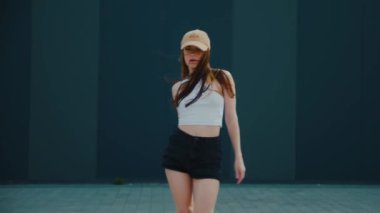 Binanın önünde dans eden bir kadın. Yavaş çekim. Beyaz bluzlu ve siyah şortlu bir kadın binanın önünde poz veriyor. Mimari arka planda sokak dansı pozu. Modern bir binanın yanında şehir dansı havası var. Şık bir kadın.