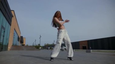 Kadın şehir binasının önünde zarif bir şekilde yüksek topuklularla dans ediyor. Enerjik kadın dışarıda dans gösterisi yapıyor. Dansçı şehrin arka planında neşe ifade ediyor. Kadın dansçı şehir planıyla büyülenir. Neşeli kadın dans yeteneklerini sergiliyor. 