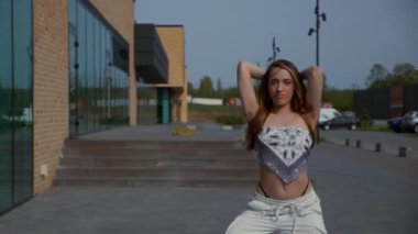 Kadın şehir binasının önünde yüksek topuklularla zarif bir şekilde dans ediyor. Yavaş çekim. Enerjik kadın dışarıda dans gösterisi yapıyor. Dansçı şehrin arka planında neşe ifade ediyor. Kadın dansçı şehir planıyla büyülenir. Neşeli kadın. 