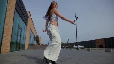 Kadın şehir binasının önünde yüksek topuklularla zarif bir şekilde dans ediyor. Yavaş çekim. Enerjik kadın dışarıda dans gösterisi yapıyor. Dansçı şehrin arka planında neşe ifade ediyor. Kadın dansçı şehir planıyla büyülenir. Neşeli kadın. 