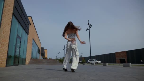 女人穿着高跟鞋优雅地在城市建筑前跳舞 慢镜头拍摄 一个精力充沛的女人在户外表演舞蹈 在城市背景下表现出欢乐的舞者 女舞蹈演员被城市景观背景所吸引 快乐的女人 — 图库视频影像