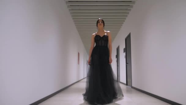 廊下を散策する黒いドレスのエレガントな女性 廊下を歩いている黒い服装のスタイリッシュな女性 彼女が通路に沿って移動するように黒い服装で優雅さを除く女性 黒い布団の女性は優雅に廊下をナビゲート — ストック動画