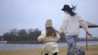 Anne ve kızı kumlu sahilde koşuyorlardı. Aile bağları deniz kenarında hareket halinde. Anne ve kızıyla birlikte tasasız bir şekilde kıyı şeridi boyunca koştu. Anne ve çocuk arasında neşeli bir sahil koşusu. Anne ve kızı mutlu bir şekilde koşuyor.