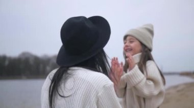 Anne ve kızı su kenarında birbirlerine sarılıp duruyorlar. Kadın ve çocuğun manzaranın tadını çıkardığı plaj sahnesi. Kadın ve kız gülümsüyor ve sahilde duruyor, denize bakıyor. Kadın ve küçük kız sahilde ufka bakıyor. Kumlu sahilde aile zamanı