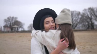 Anne ve kızı su kenarında birbirlerine sarılıp duruyorlar. Kadın ve çocuğun manzaranın tadını çıkardığı plaj sahnesi. Kadın ve kız gülümsüyor ve sahilde duruyor, denize bakıyor. Kadın ve küçük kız sahilde ufka bakıyor. Kumlu sahilde aile zamanı