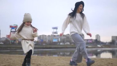 Anne ve kızı kumlu sahilde koşuyorlardı. Aile bağları deniz kenarında hareket halinde. Anne ve kızıyla birlikte tasasız bir şekilde kıyı şeridi boyunca koştu. Anne ve çocuk arasında neşeli bir sahil koşusu. Anne ve kızı mutlu bir şekilde koşuyor.