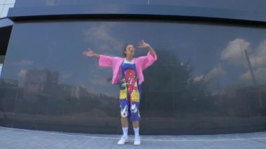 Tuhaf pembe elbiseli bir kadın binanın önünde neşeyle dans ediyor. Pembe elbiseli canlı bir kadın bir binanın yakınında dans figürleri sergiliyor. Pembe ceketli ve şortlu biri bir binanın yanında dans ediyor. Pembeli, neşeli bir kadın. 