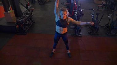 Beden eğitiminde fiziksel egzersiz yapan bir kadın. Kadın spor salonunda ağırlıklı çömelme yapıyor. Aktif bayan spor salonunda dambıllarla çömeliyor. Kadın bacak egzersizi için çömeliyor. Spor meraklısı düzgün bir şekilde çömeliyor. Sportif Kadın  