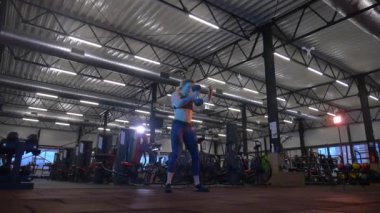 Beden eğitiminde fiziksel egzersiz yapan bir kadın. Kadın spor salonunda ağırlıklı çömelme yapıyor. Aktif bayan spor salonunda dambıllarla çömeliyor. Kadın bacak egzersizi için çömeliyor. Spor meraklısı düzgün bir şekilde çömeliyor. Sportif Kadın  