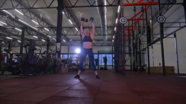 Beden eğitiminde fiziksel egzersiz yapan bir kadın. Kadın spor salonunda ağırlıklı çömelme yapıyor. Aktif bayan spor salonunda dambıllarla çömeliyor. Kadın bacak egzersizi için çömeliyor. Spor meraklısı düzgün bir şekilde çömeliyor. Sportif Kadın  