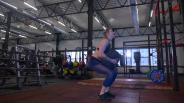 Beden eğitiminde fiziksel egzersiz yapan bir kadın. Kadın spor salonunda ağırlıklı çömelme yapıyor. Aktif bayan spor salonunda dambıllarla çömeliyor. Kadın bacak egzersizi için çömeliyor. Spor meraklısı düzgün bir şekilde çömeliyor. Sportif Kadın  