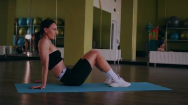 Bir kadın fiziksel egzersiz yapıyor. Genç bir kız kaslarını esneterek hücum eder. Spor salonunda spor mankeni. Güzel vücutlu bir kadın paspasın üzerinde fiziksel egzersiz yapar.. 