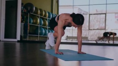 Bir kadın fiziksel egzersiz yapıyor. Genç bir kız kaslarını esneterek hücum eder. Spor salonunda spor mankeni. Güzel vücutlu bir kadın paspasın üzerinde fiziksel egzersiz yapar.. 