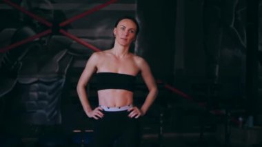 Spor salonunda çalışan ve kameraya poz veren bir kız. Seksi kadın model spor salonunda simülatörlere bağlanır. Güzel spor figürü..