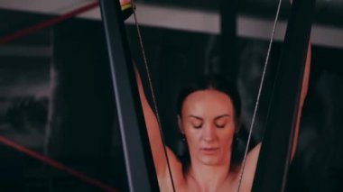 Spor salonunda çalışan ve kameraya poz veren bir kız. Seksi kadın model spor salonunda simülatörlere bağlanır. Güzel spor figürü..