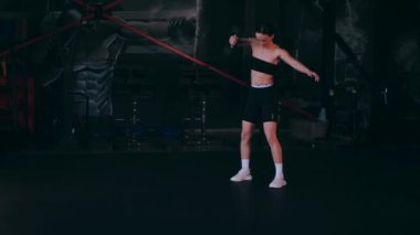 Spor salonunda dambıllı bir kız antrenman yapıyor. Seksi kadın model spor salonunda simülatörlere bağlanır. Güzel spor figürü..