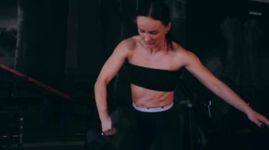 Spor salonunda dambıllı bir kız antrenman yapıyor. Seksi kadın model spor salonunda simülatörlere bağlanır. Güzel spor figürü..