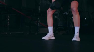 Spor salonunda dambıllı bir kız antrenman yapıyor. Seksi kadın model spor salonunda simülatörlere bağlanır. Güzel spor figürü..