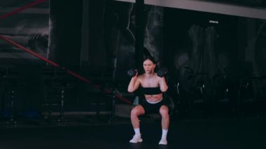 Spor salonunda dambıllı bir kız antrenman yapıyor. Seksi kadın model spor salonunda simülatörlere bağlanır. Güzel spor figürü..