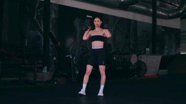 Spor salonunda dambıllı bir kız antrenman yapıyor. Seksi kadın model spor salonunda simülatörlere bağlanır. Güzel spor figürü..