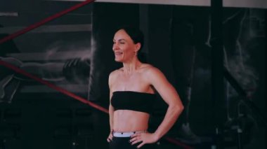 Spor salonunda çalışan ve kameraya poz veren bir kız. Seksi kadın model spor salonunda simülatörlere bağlanır. Güzel spor figürü..