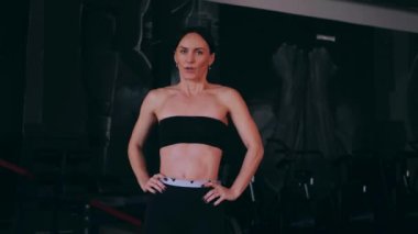 Spor salonunda çalışan ve kameraya poz veren bir kız. Seksi kadın model spor salonunda simülatörlere bağlanır. Güzel spor figürü..