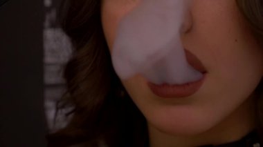 Genç bir kadın yatakta elektronik sigara içiyor. Güzel bir kadın yatağa uzanır ve baştan çıkarıcı bir şekilde kameraya bakar. Bir kadın ağzından sigara dumanı üflüyor..