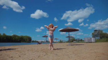Bachata, salsa ve kizomba yapan bir kadın. Sahilde, mavi gökyüzünün arka planında. Gülümseyen kadın çıplak ayakla poz verir ve sıcak kumda baştan çıkarıcı bir şekilde dans eder. Plaj sahnesinde kızın keyfi yerinde. Şortlu ve tişörtlü güzel bayan poz veriyor.