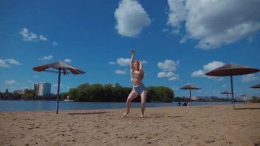 Bachata, salsa ve kizomba yapan bir kadın. Sahilde, mavi gökyüzünün arka planında. Gülümseyen kadın çıplak ayakla poz verir ve sıcak kumda baştan çıkarıcı bir şekilde dans eder. Plaj sahnesinde kızın keyfi yerinde. Şortlu ve tişörtlü güzel bayan poz veriyor.
