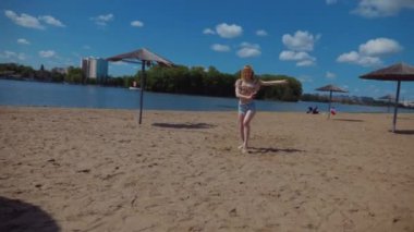 Bachata, salsa ve kizomba yapan bir kadın. Sahilde, mavi gökyüzünün arka planında. Gülümseyen kadın çıplak ayakla poz verir ve sıcak kumda baştan çıkarıcı bir şekilde dans eder. Plaj sahnesinde kızın keyfi yerinde. Şortlu ve tişörtlü güzel bayan poz veriyor.