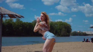 Bachata, salsa ve kizomba yapan bir kadın. Sahilde, mavi gökyüzünün arka planında. Gülümseyen kadın çıplak ayakla poz verir ve sıcak kumda baştan çıkarıcı bir şekilde dans eder. Plaj sahnesinde kızın keyfi yerinde. Şortlu ve tişörtlü güzel bayan poz veriyor.