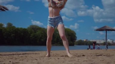 Bachata, salsa ve kizomba yapan bir kadın. Sahilde, mavi gökyüzünün arka planında. Gülümseyen kadın çıplak ayakla poz verir ve sıcak kumda baştan çıkarıcı bir şekilde dans eder. Plaj sahnesinde kızın keyfi yerinde. Şortlu ve tişörtlü güzel bayan poz veriyor.