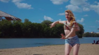 Bachata, salsa ve kizomba yapan bir kadın. Sahilde, mavi gökyüzünün arka planında. Gülümseyen kadın çıplak ayakla poz verir ve sıcak kumda baştan çıkarıcı bir şekilde dans eder. Plaj sahnesinde kızın keyfi yerinde. Şortlu ve tişörtlü güzel bayan poz veriyor.