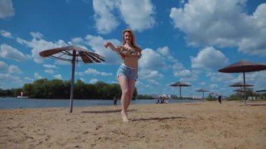 Bachata, salsa ve kizomba yapan bir kadın. Sahilde, mavi gökyüzünün arka planında. Gülümseyen kadın çıplak ayakla poz verir ve sıcak kumda baştan çıkarıcı bir şekilde dans eder. Plaj sahnesinde kızın keyfi yerinde. Şortlu ve tişörtlü güzel bayan poz veriyor.