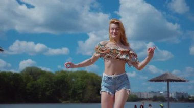 Bachata, salsa ve kizomba yapan bir kadın. Sahilde, mavi gökyüzünün arka planında. Gülümseyen kadın çıplak ayakla poz verir ve sıcak kumda baştan çıkarıcı bir şekilde dans eder. Plaj sahnesinde kızın keyfi yerinde. Şortlu ve tişörtlü güzel bayan poz veriyor.