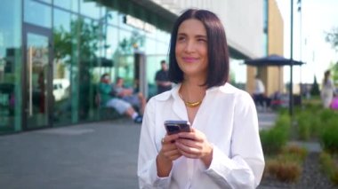 İş merkezinin yanındaki bankta oturan bir kadın telefonda konuşuyor. Ofis çalışanı, yönetmen, resmi kıyafetler. Beyaz gömlekli ve siyah pantolonlu bir kadın bankta cep telefonuyla sohbet ediyor ve caddenin karşısında gülümsüyor. Gülümseyen iş adamı oturuyor. 