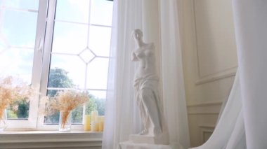 Pencerenin yanındaki zarif heykel. Parlak bir pencereye karşı heykel. Pencereden dışarı bakan heykel. Pencere kenarında tefekkür eden heykel. Heykel ile pencere görünümü